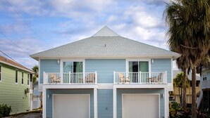 A two-story house with a balcony on the upper floor, a garage on the lower floor, and a palm tree in the background. - The Finn at Coconut Cove (Fort Myers Beach)