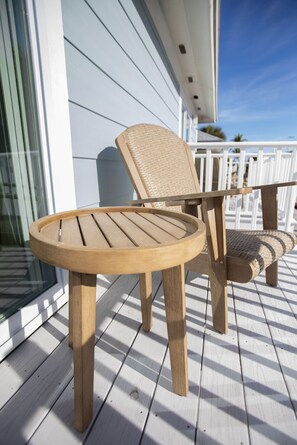 A wooden deck with a round table and a chair, white railings, and a building with large windows. - The Finn at Coconut Cove (Fort Myers Beach)