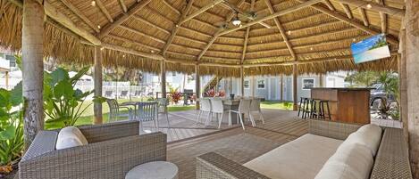 Un espacio de estar techado al aire libre con muebles de mimbre y techo de paja.