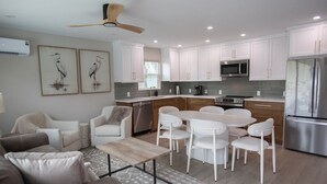 A modern kitchen with white cabinets, stainless steel appliances, and a dining area with white chairs. - The Finn at Coconut Cove (Fort Myers Beach)