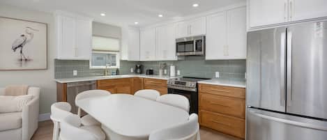 Una cocina moderna con muebles blancos, un refrigerador de acero inoxidable y un comedor con mesa y sillas blancas.