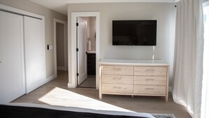 A bedroom with a bed, a dresser, a TV, and a door leading to a bathroom. - The Finn at Coconut Cove (Fort Myers Beach)