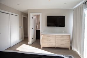 Ein Schlafzimmer mit einem Bett, einem Schminktisch, einem Fernseher und einer Tür zu einem Badezimmer.