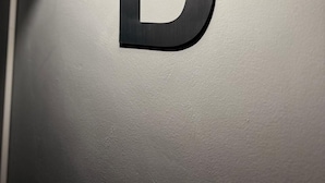 Une lettre « D » en métal, illuminée par un projecteur sur un mur.