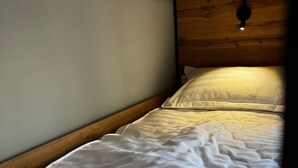 Un lit simple avec une tête de lit en bois, dans une pièce dont le plafond est en pente.