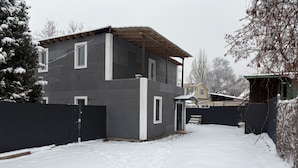 Une maison à deux étages, avec une façade en briques sombres, un porche abrité et une allée recouverte de neige.