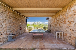 A stone-walled outdoor area with a ping pong table, two small tables, and a pergola structure.