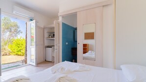 Ein Hotelzimmer mit Bett, einem Badezimmer mit blauen Fliesen, einer kleinen Küchenzeile und einer Schiebetür zum Außenbereich.