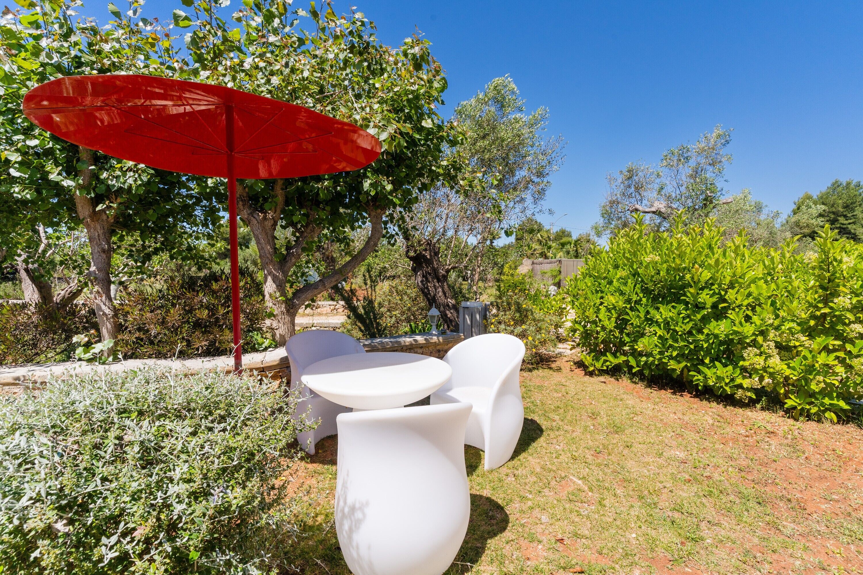 Une terrasse dotée de mobilier blanc, d’un parasol rouge et d’une végétation luxuriante.