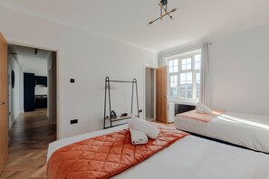 A hotel room with two beds, a wooden floor, a window with curtains, and a hanging shoe rack. - Bright Apartments near Hyd Park (London)