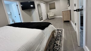 Een slaapkamer met een bed, een tv aan de muur, een stoel, een kledingkast en een deur naar een andere kamer.