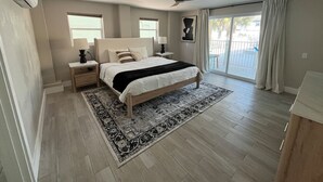 Een slaapkamer met een bed, nachtkastjes, een plafondventilator en een groot raam.