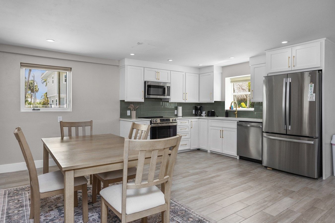 A modern kitchen with white cabinets, stainless steel appliances, and a dining area with a wooden table and chairs.