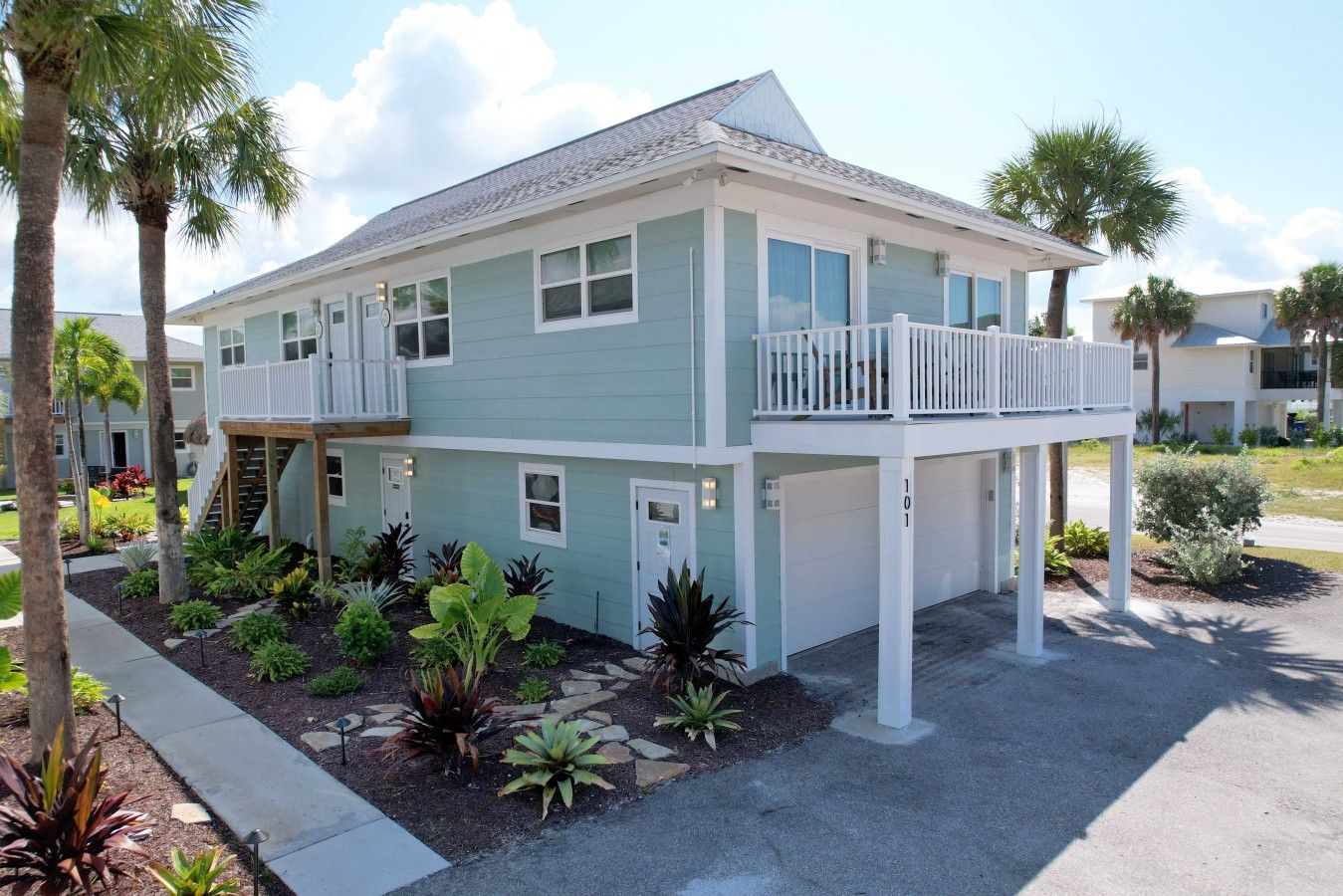 A two-story building with a balcony, a covered porch, and a landscaped garden with various plants.