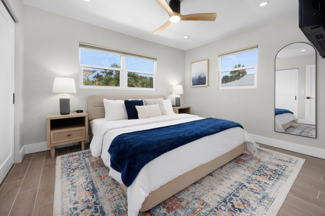 A bedroom with a bed, bedside tables, a ceiling fan, and a large mirror.