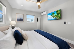 A modern bedroom with a bed, a ceiling fan, a TV, and a window. - The Dex at Coconut Cove (Fort Myers Beach)