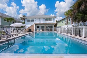 A swimming pool with a clear blue sky and clouds in the background, surrounded by a white fence and palm trees. - The Dex at Coconut Cove (Fort Myers Beach)
