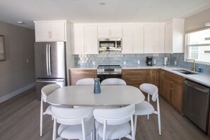 Een moderne keuken met witte kasten, roestvrijstalen apparatuur, een ronde eettafel met stoelen en een betegelde achterwand.