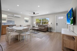 A modern living room with a dining area, a sofa, and a TV mounted on the wall. - The Wren at Coconut Cove (Fort Myers Beach)