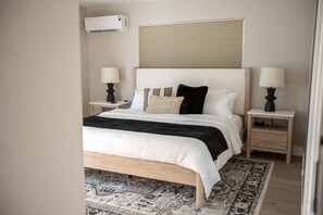 Een slaapkamer met een bed, twee nachtkastjes, een wandairconditioner en een raam met zonwering.