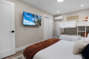 A hotel room with a bed, a bunk bed, a television, and an air conditioning unit. - The Wren at Coconut Cove (Fort Myers Beach)