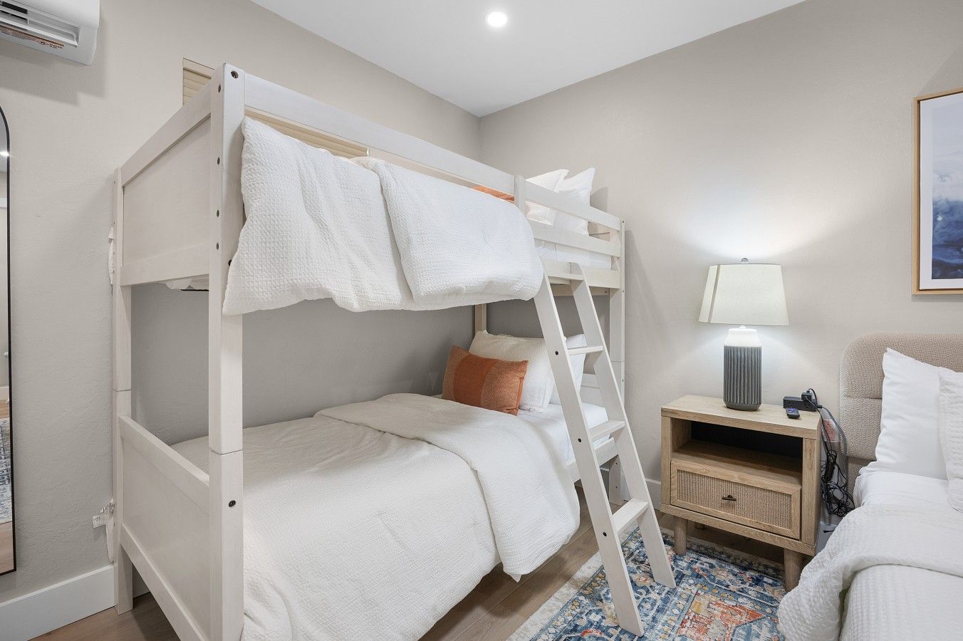 Un lit superposé avec une échelle, une table de chevet avec une lampe et un tapis à motifs.