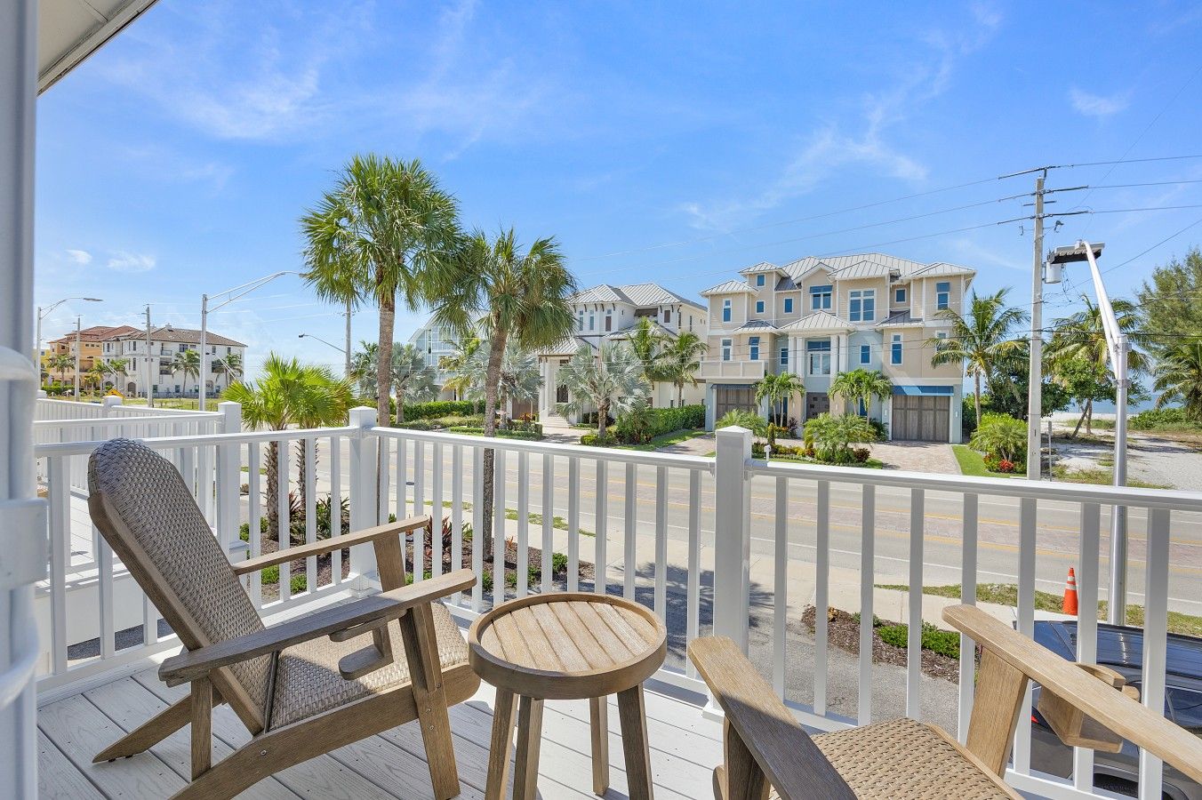 A wooden deck with a chair and table, overlooking a street with multi-story buildings and palm trees.