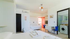 Habitación de hotel con cama, escritorio, silla, lavadora y baño visible a través de una puerta abierta.