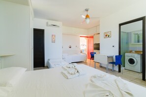 A hotel room with a bed, a desk, a chair, a washing machine, and a bathroom visible through an open door. - Apartment 'Core Resort - Familiare Bianca' with Shared Pool, Wi-Fi and Air Conditioning (Tuglie)
