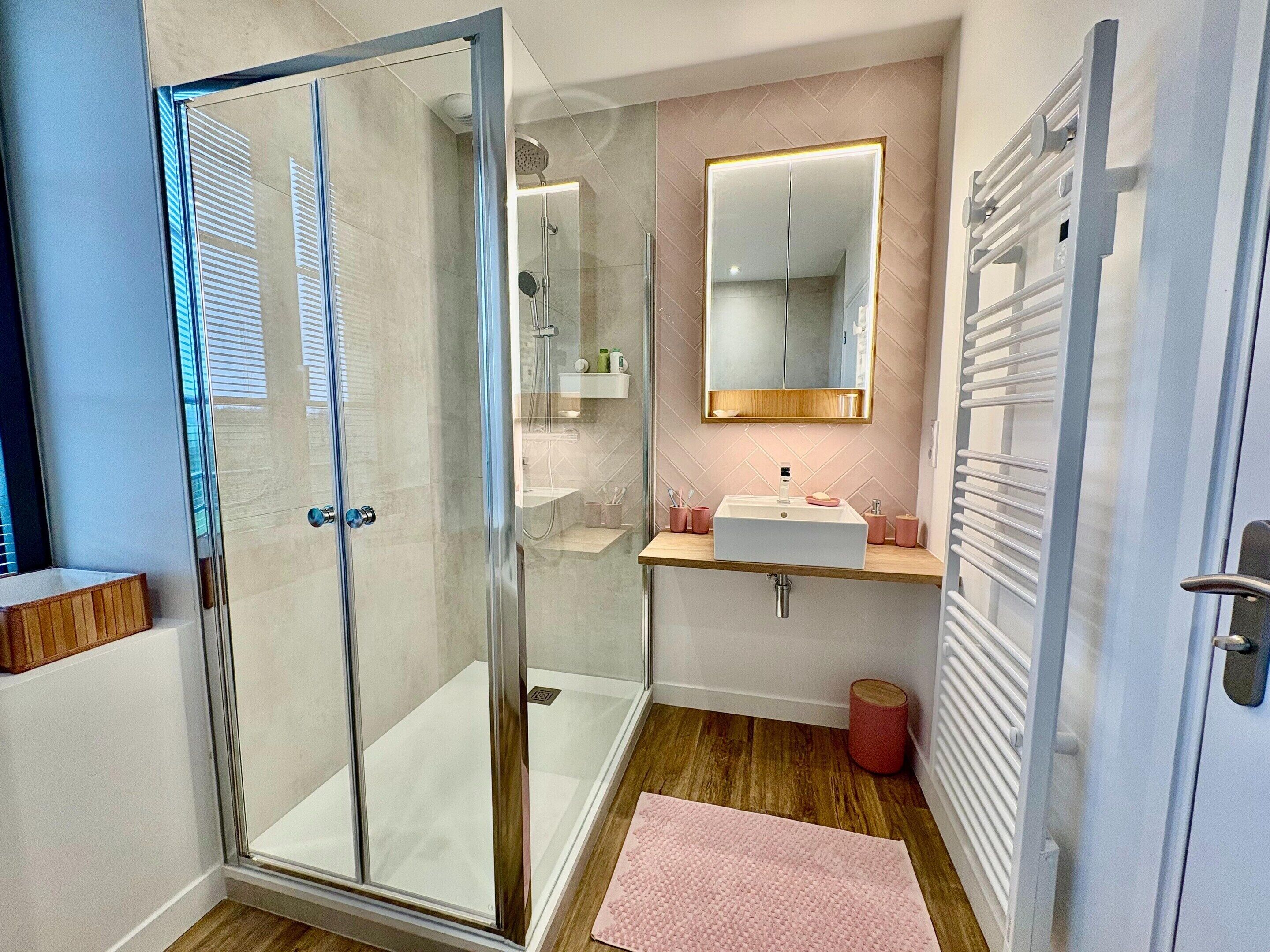 A modern bathroom with a glass shower enclosure, a vanity with a mirror, and a wooden floor.