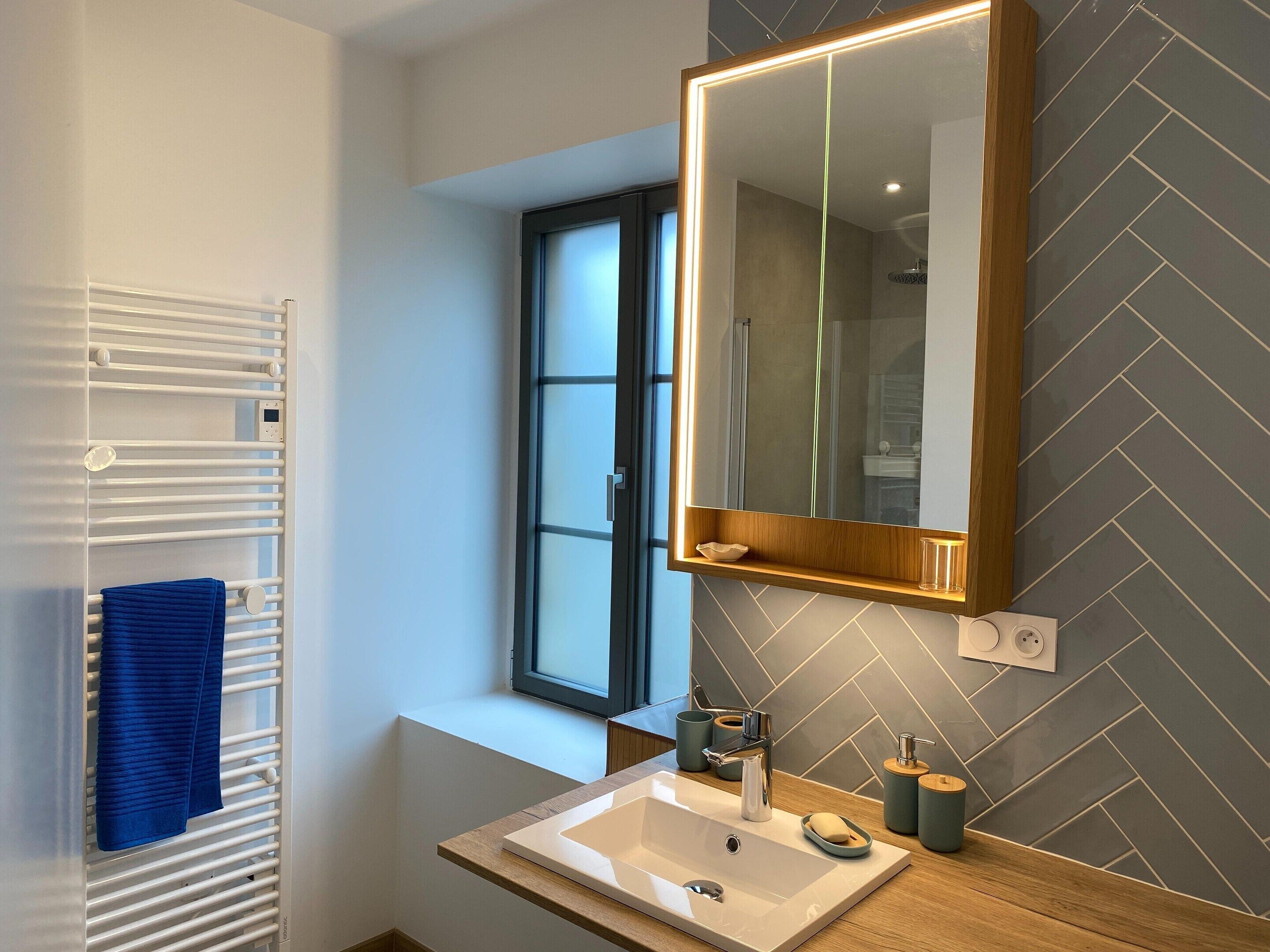 A modern bathroom with a white sink, a mirror, and a window.