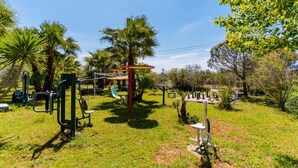 Zona de gimnasio al aire libre con equipo de ejercicio, un tobogán y palmeras.