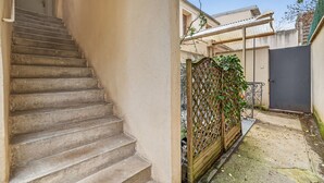 Una escalera de acceso a una vivienda, un patio trasero amurallado con cerca de madera, y un edificio con techo de metal.