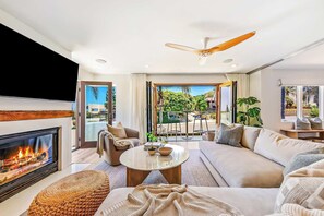 A modern living room with a fireplace, a ceiling fan, and a view of the outdoors. - The Sea & Sand - Ocean View La Jolla Condo (San Diego)
