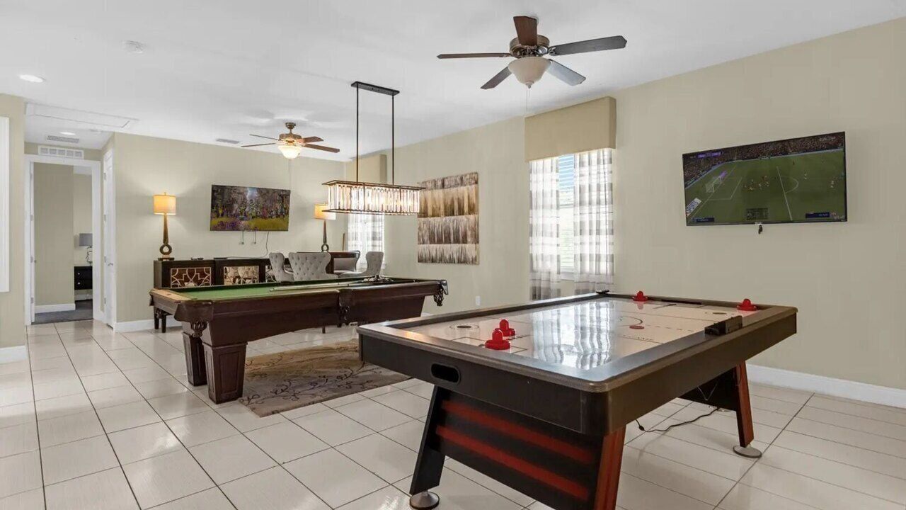 Une pièce spacieuse équipée d’une table de billard, d’une autre table et d’un ventilateur de plafond.