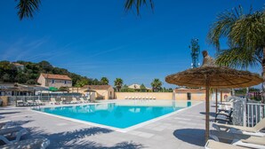 A swimming pool with lounge chairs, a thatched umbrella, and palm trees. - “3-Bedroom Mobile Home in St Aygulf” with Shared Pool, Wi-Fi, and Air Conditioning (Fréjus)