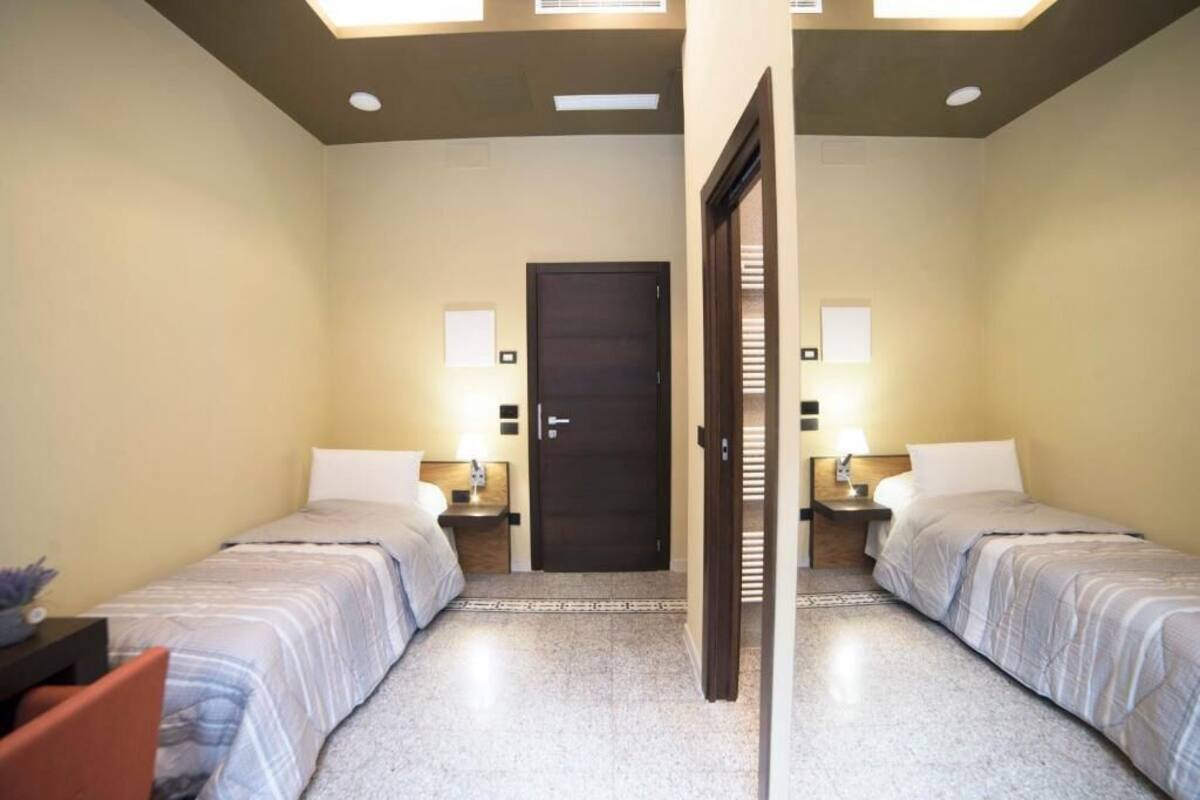 A hotel room with two beds, a dark door, and two bedside tables with lamps.
