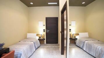 Une chambre d’hôtel avec deux lits, une porte sombre et deux tables de chevet avec des lampes.