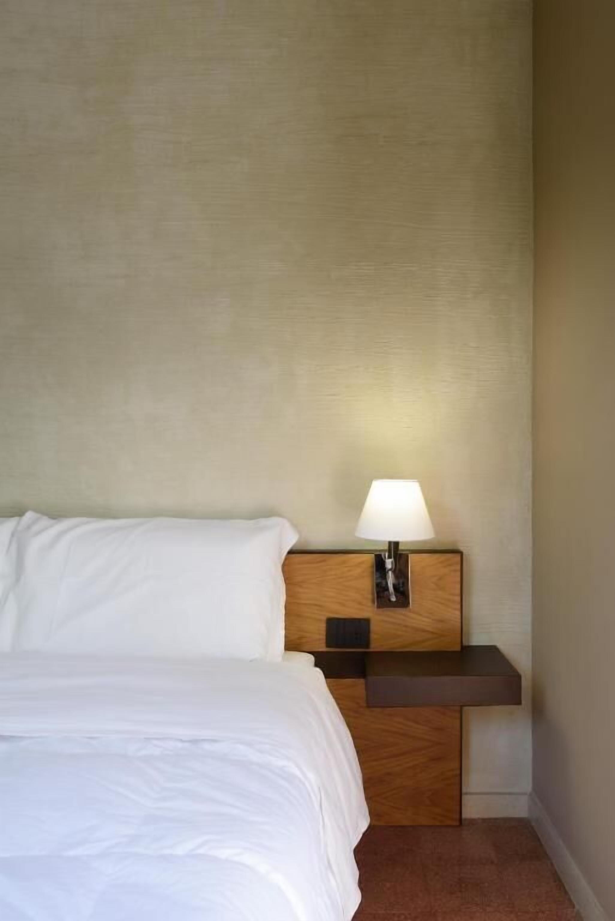 Una habitació d'hotel amb un llit, una tauleta de nit amb una làmpada i un panell de fusta al capçal.