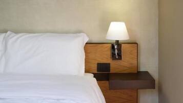 Una habitació d'hotel amb un llit, una tauleta de nit amb una làmpada i un panell de fusta al capçal.