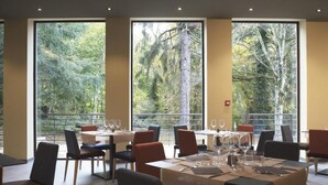 Een restaurant met gedekte tafels, grote ramen met uitzicht op een bos en een modern interieur.