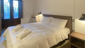 Een slaapkamer met een houten plafond, een bed met witte beddengoed, een nachtkastje en een raam met gordijnen.