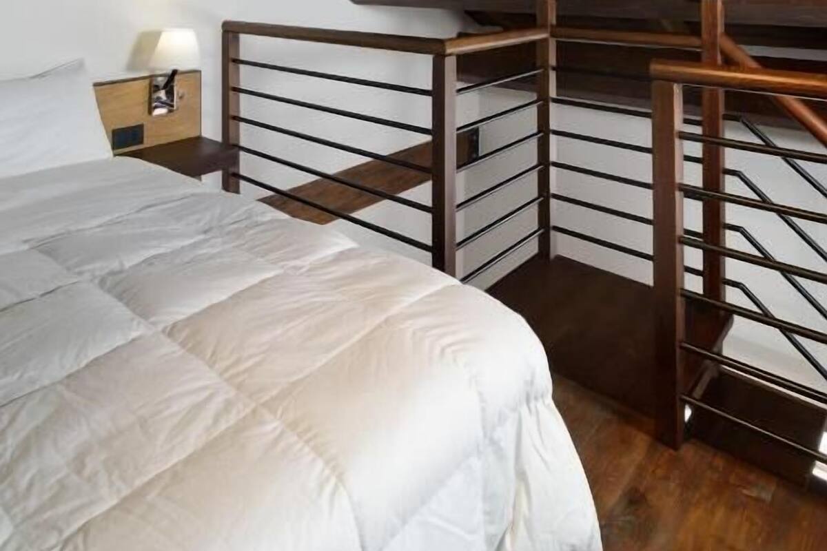 A bedroom with a wooden ceiling, a bed with a white comforter, and a nightstand with a lamp.