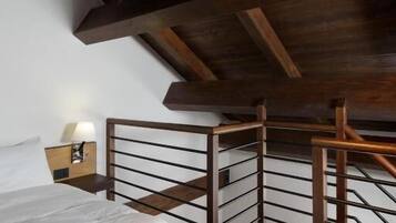 Un dormitorio con techo de madera, una cama con edredón blanco y una mesita de noche con lámpara.