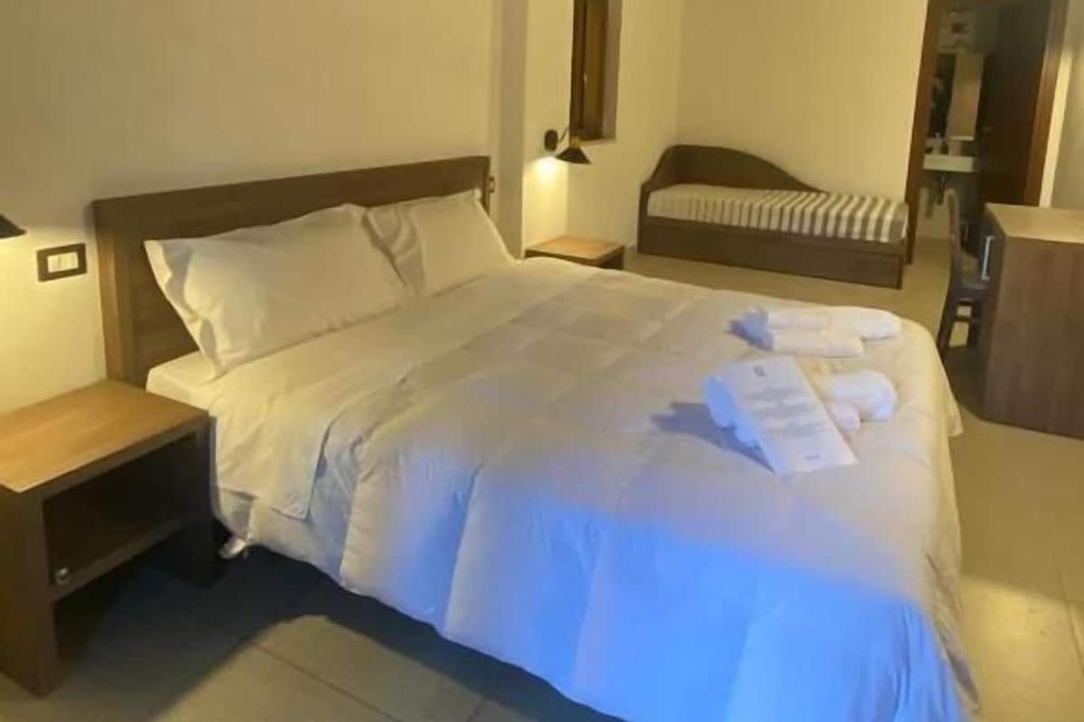 A bedroom with a large bed, a nightstand, a wooden ceiling, and a small table.