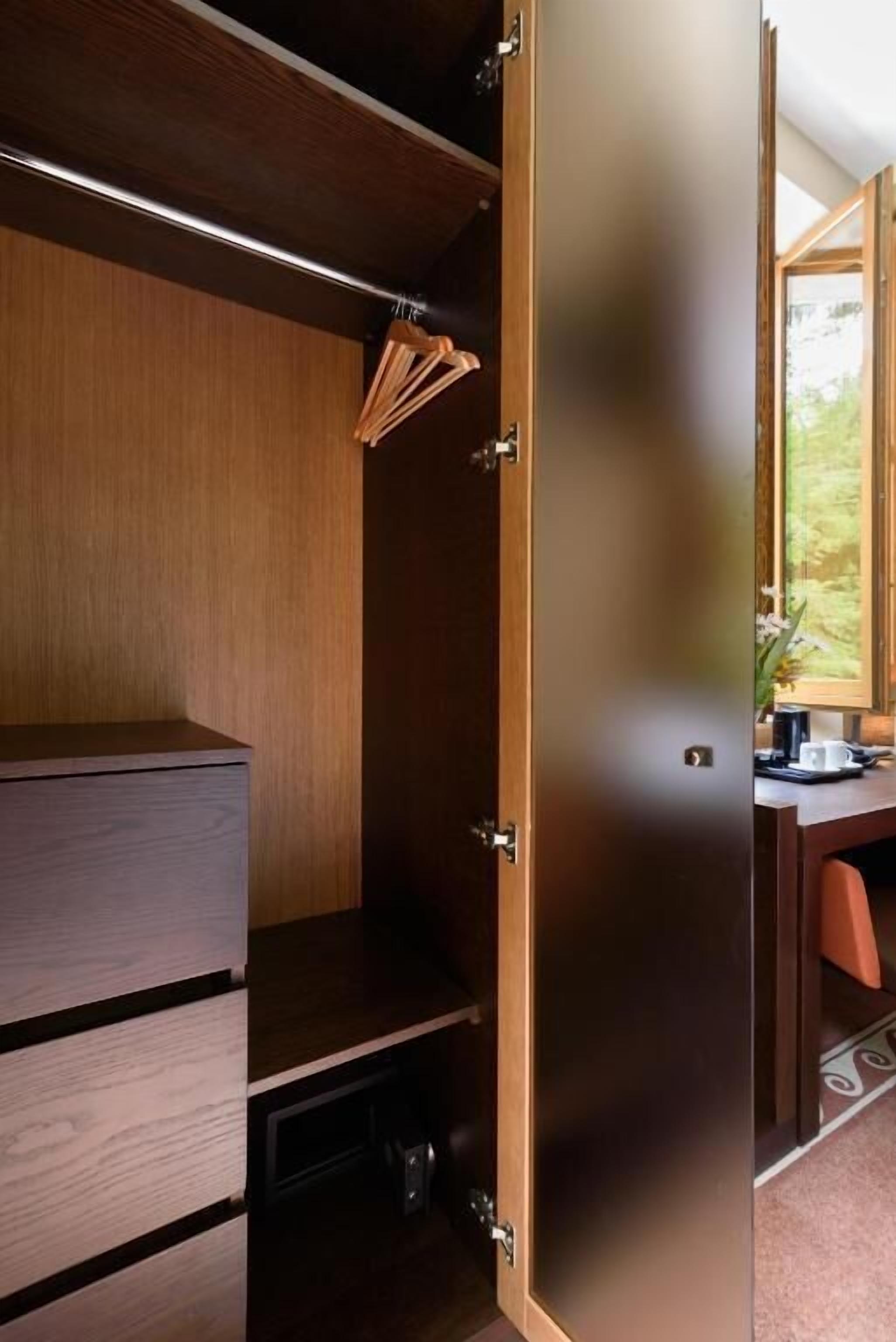 Habitación compacta con un armario de madera, un escritorio con silla, y una ventana con vistas a zonas verdes.
