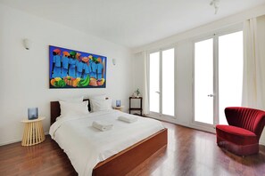 A hotel room with a large bed, a red armchair, a painting on the wall, and a sliding glass door. - Beautiful Apartment in the Marais - 3bdr/6p - Paris (Paris)
