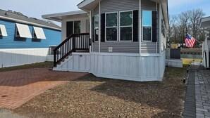 A single-story house with a covered porch, a small staircase, and a flagpole with an American flag.
