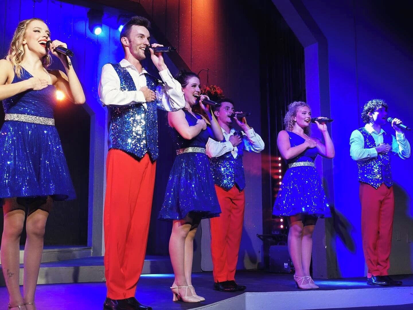 A group of people on a stage with microphones, wearing sequined outfits.