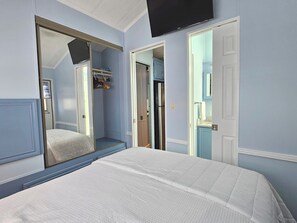 A bedroom with a bed, a television mounted on the wall, and a walk-in closet.